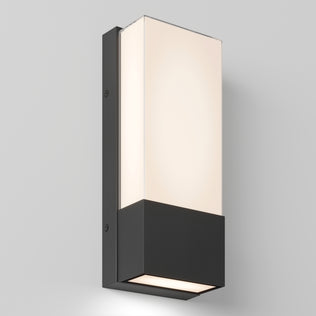 The Artika Dixon indoor-outdoor LED wall light features a modern rectangular design with a black base and frosted white glass shade, mounted on a light gray wall and emitting soft, even illumination.