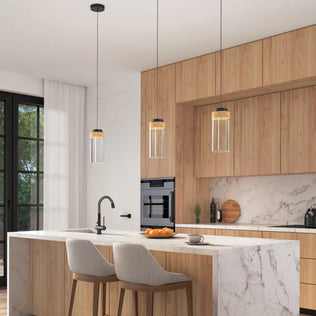 Modern kitchen with light wood cabinets, marble island and backsplash, two upholstered bar stools, a built-in oven, large windows overlooking greenery, and three Artika Hanson 1-light LED pendant 5 CCT lights above the island.
