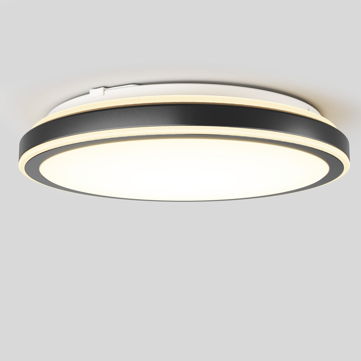A modern round ceiling light fixture with a black and gold trim, featuring a wide, illuminated white center against a plain gray background.