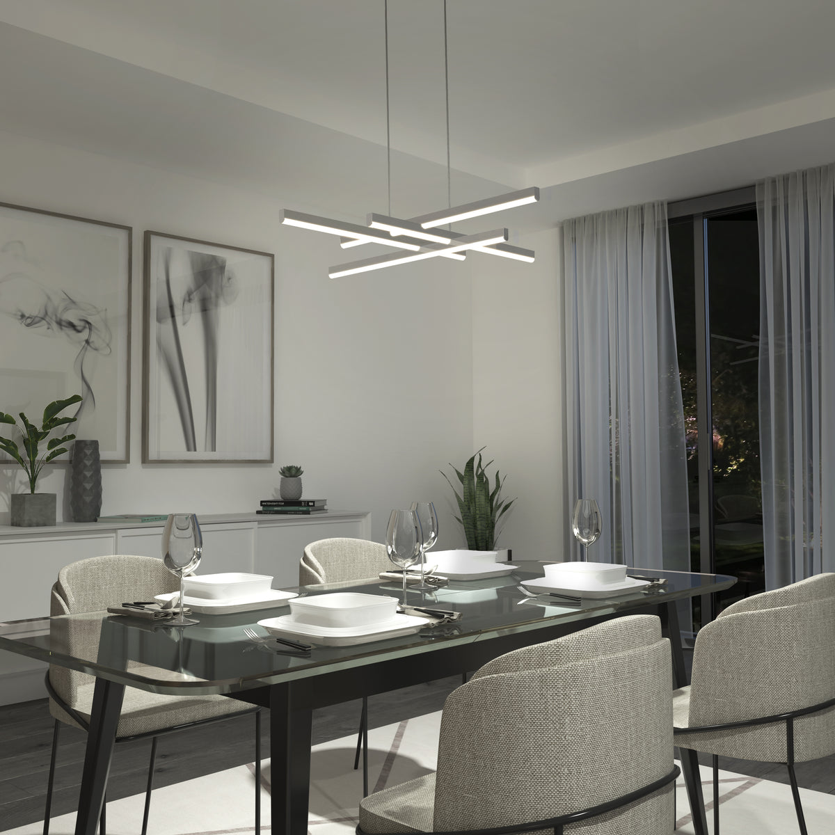 A modern dining room with a glass table set for four, beige upholstered chairs, abstract wall art, plants, and a geometric LED chandelier. Floor-length sheer curtains cover large windows at night.