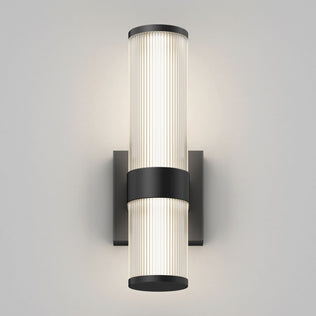 The Artika Mirado modern LED wall sconce 5 CCT features two vertically stacked cylindrical diffusers, a black central band, and a black rectangular base, offering a soft, even glow against a light gray wall.