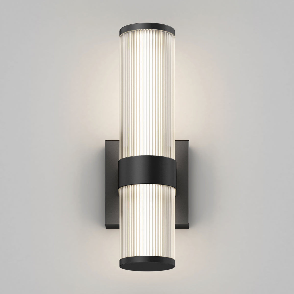 Wall-mounted modern sconce with two cylindrical, vertically stacked frosted glass lights, separated and accented by a central black metal band and cap, illuminating a neutral background.