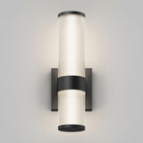 Wall-mounted modern sconce with two cylindrical, vertically stacked frosted glass lights, separated and accented by a central black metal band and cap, illuminating a neutral background.