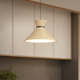 A modern pendant lamp with a light wood finish hangs from the ceiling in a kitchen with beige panel walls and a textured brown backsplash.