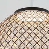 Close-up of a woven rattan lampshade with a crisscross pattern, illuminated from within and hanging from the ceiling by a black cord, against a light background.