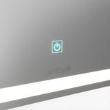 A close-up of a mirror featuring a glowing blue power button symbol, the artika logo below it, and a white horizontal LED light strip at the bottom.