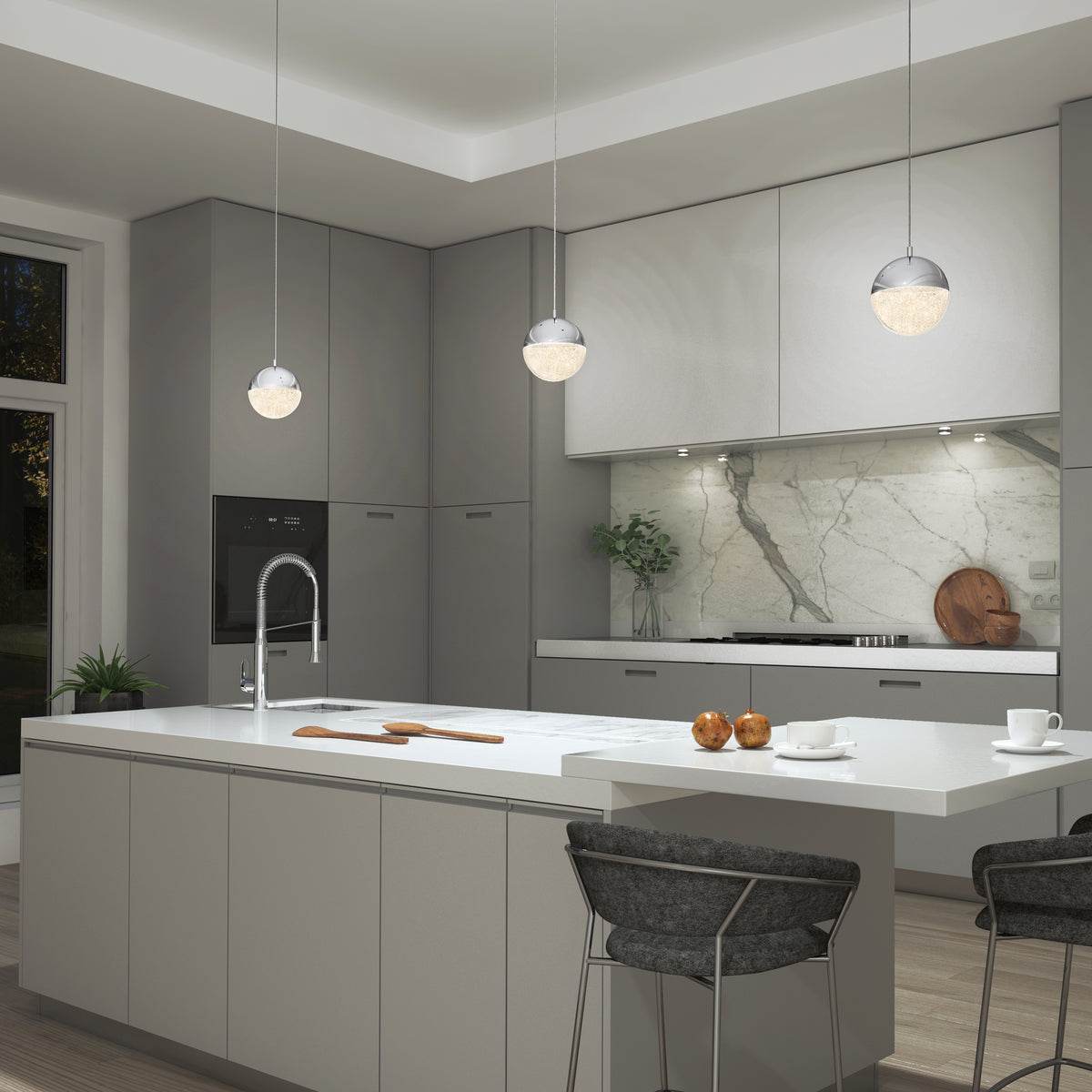 Modern kitchen with gray cabinets, white countertops, marble backsplash, and a large island with a sink. Three Artika Sparkle 1 light LED pendants hang above the island, which has two bar stools and apples on the counter.
