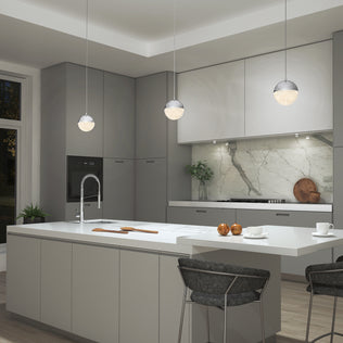 Modern kitchen with gray cabinets, white countertops, marble backsplash, and a large island with a sink. Three Artika Sparkle 1 light LED pendants hang above the island, which has two bar stools and apples on the counter.