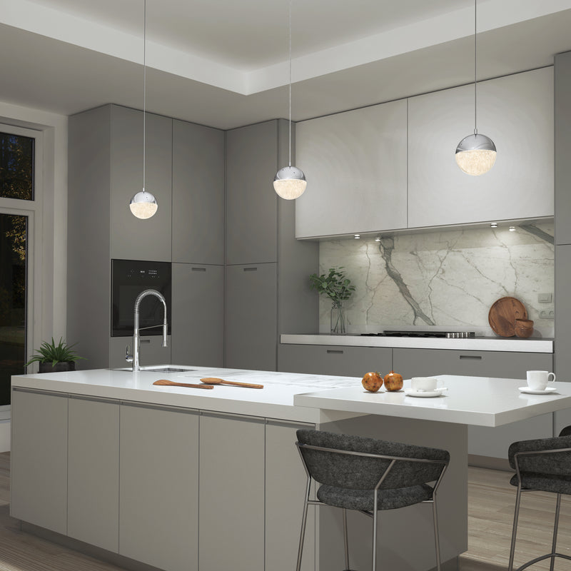 Modern kitchen with gray cabinets, white countertops, marble backsplash, and a large island with a sink. Three Artika Sparkle 1 light LED pendants hang above the island, which has two bar stools and apples on the counter.