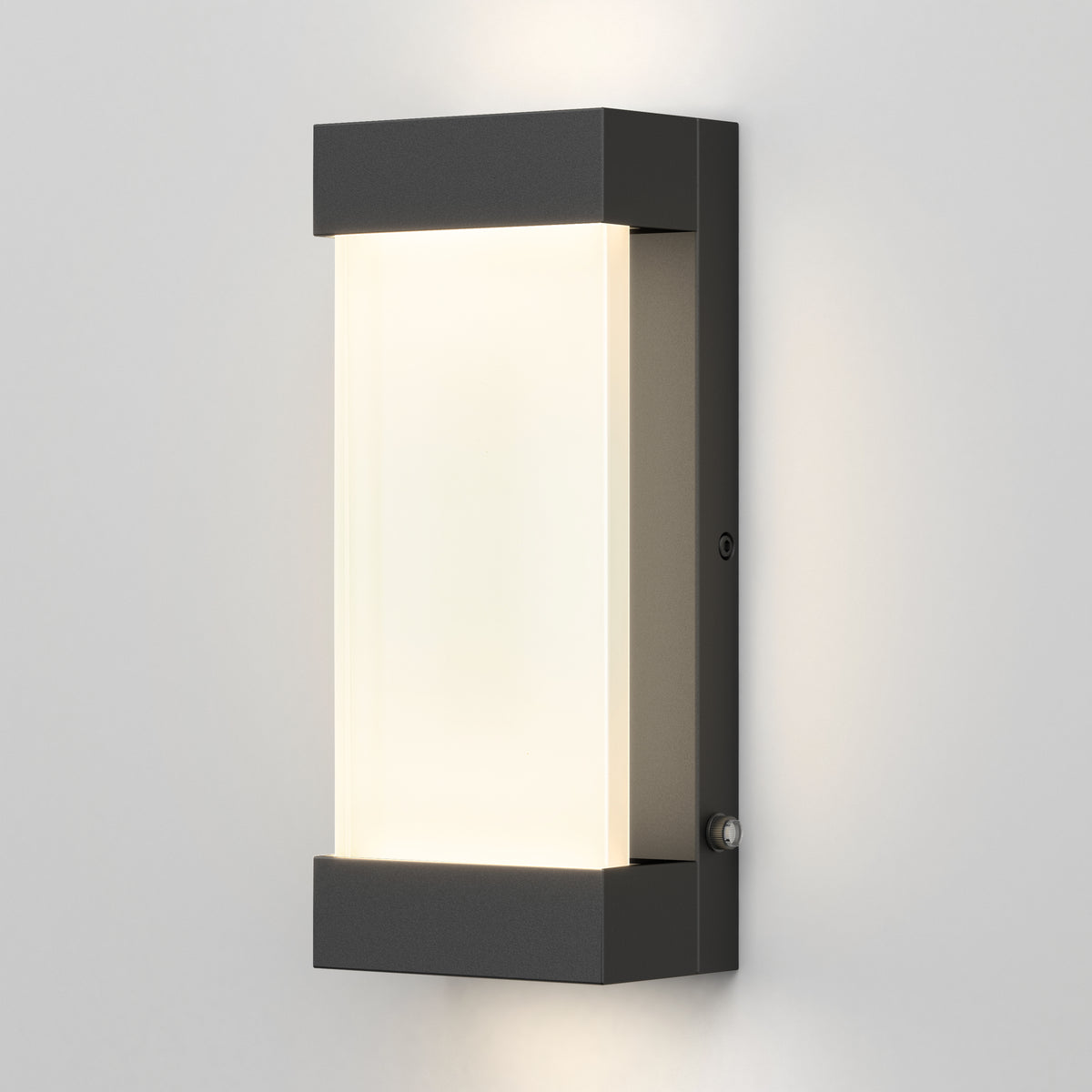 A modern rectangular wall sconce with a black frame and frosted white center panel, mounted on a light gray wall and emitting a soft, even glow.