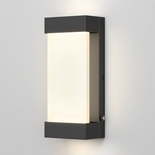 The Artika Glacier indoor-outdoor LED wall light features a modern rectangular black metal frame with a frosted white center, mounted on a light gray wall and emitting a soft edge glow.
