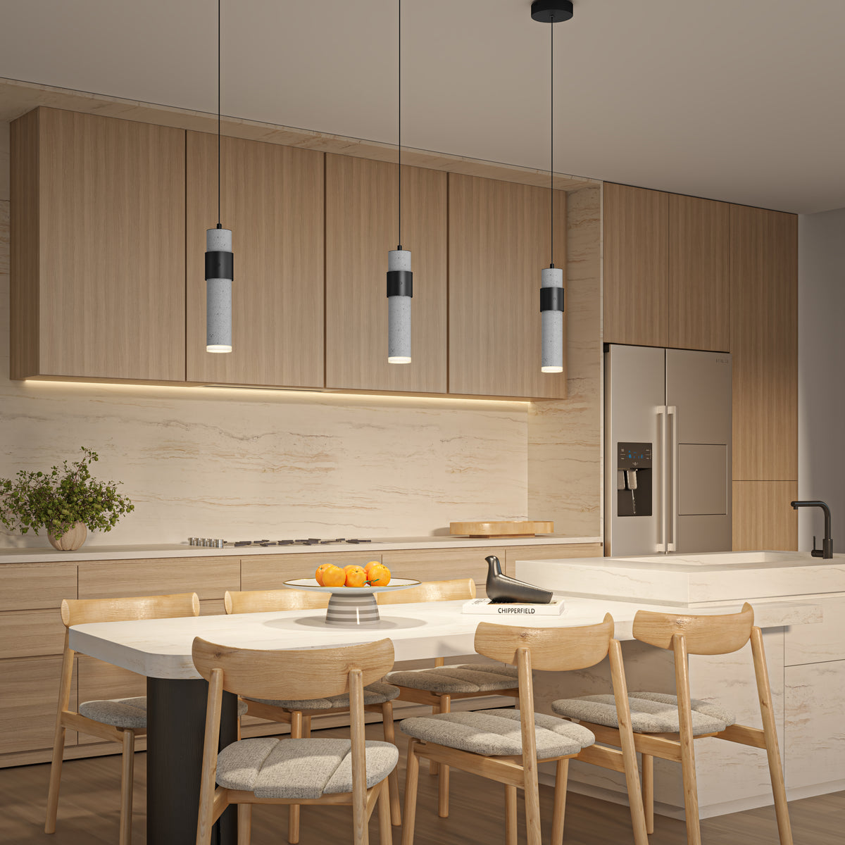 Modern kitchen with light wood cabinets, marble backsplash, and an island with a sink. Four wooden chairs surround a dining table with oranges. Above the island hang three Artika Barden 1-light LED pendant 5 CCT lights.