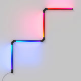 A modern LED wall light with four connected segments forming a zigzag pattern, each segment glowing in vibrant colors including red, pink, blue, and orange, mounted on a plain light-colored wall.