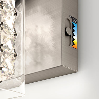 Close-up of a metallic wall-mounted fixture with a textured glass element on the left and a small colorful label with triangular graphics on the right side of the metal surface.