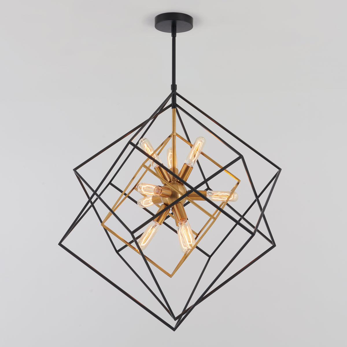 A modern geometric chandelier with black and gold cube frames intersecting, surrounding exposed vintage-style light bulbs, hanging from a black ceiling mount against a plain white background.