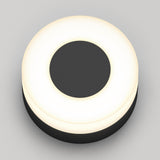 A round, black object with a glowing white ring around its edge, resembling a modern ceiling or wall light fixture, set against a plain gray background.