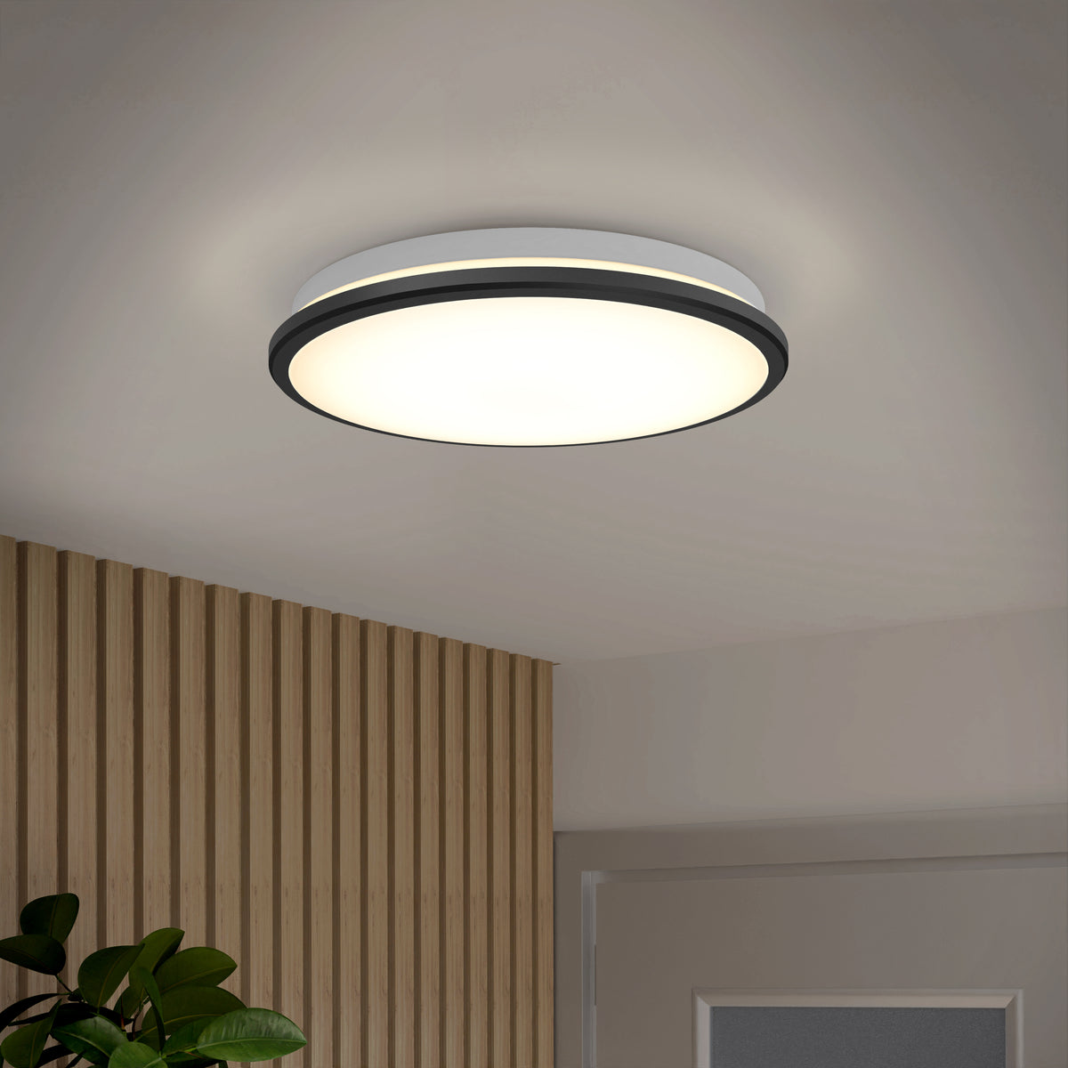 The Artika Vera 13 in. Modern LED Flush Mount ceiling light shines in a wood-paneled room with a door and leafy plant.