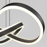 A close-up of a modern, abstract LED pendant light with curved, intertwined black and white illuminated bands suspended by thin wires against a plain gray background.