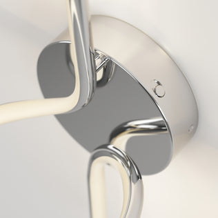 Close-up of Artikas Swirl LED Sconce: a sleek, contemporary wall fixture with a glossy chrome finish, circular base, and curved arms, adding modern style and reflective shine to any light-colored wall.