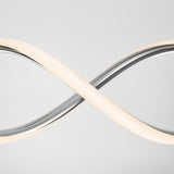 A modern light fixture shaped like an infinity symbol, with a sleek metallic finish and glowing white light, set against a plain light gray background.