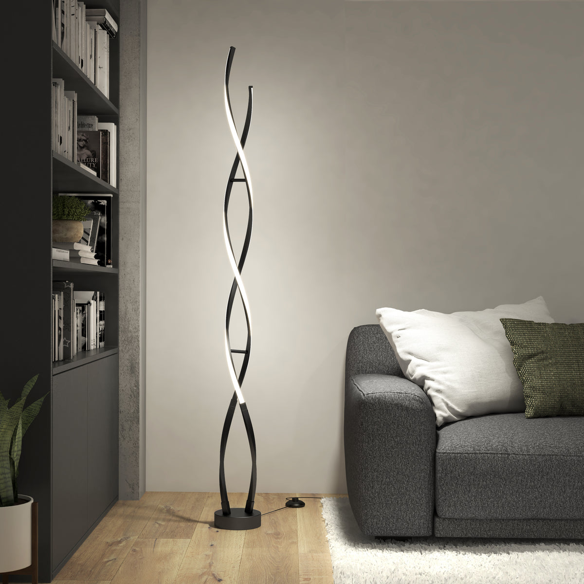 Modern living room with a gray sofa, green and white pillows, a plant, bookshelves, and a tall, spiral-shaped black floor lamp emitting soft white light against a light-colored wall on a wooden floor.