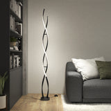Modern living room with a gray sofa, green and white pillows, a plant, bookshelves, and a tall, spiral-shaped black floor lamp emitting soft white light against a light-colored wall on a wooden floor.