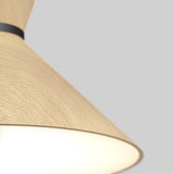 Close-up of a modern light fixture with a conical, light wood-textured shade and black band, emitting a soft white glow against a plain light gray background.