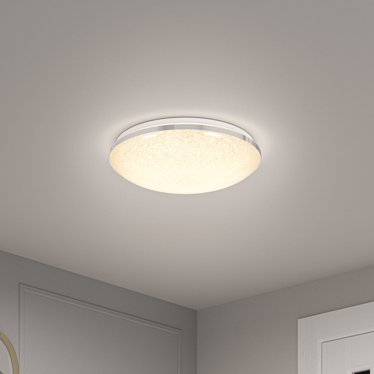 A modern, round flush mount ceiling light with a frosted, slightly textured cover emits a warm glow in a neutral-toned room with light gray walls and white trim.