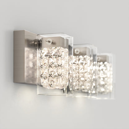 A modern wall-mounted light fixture with three rectangular lamps, each featuring clear crystal-like embellishments and a silver metallic base, emitting a bright, elegant glow.