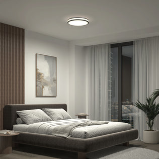 Modern bedroom with low bed, abstract wall art, Artika Hemisphere LED ceiling light, and a city view through floor-to-ceiling windows.