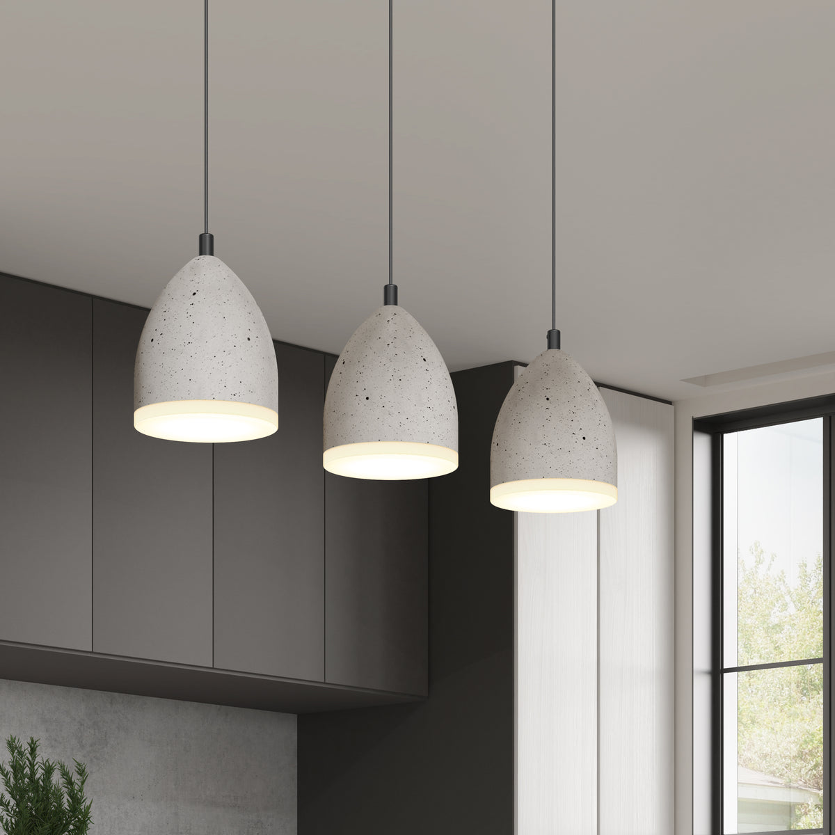 Three modern, cone-shaped pendant lights with a concrete finish hang from the ceiling in a minimalistic kitchen with dark cabinets and large windows.