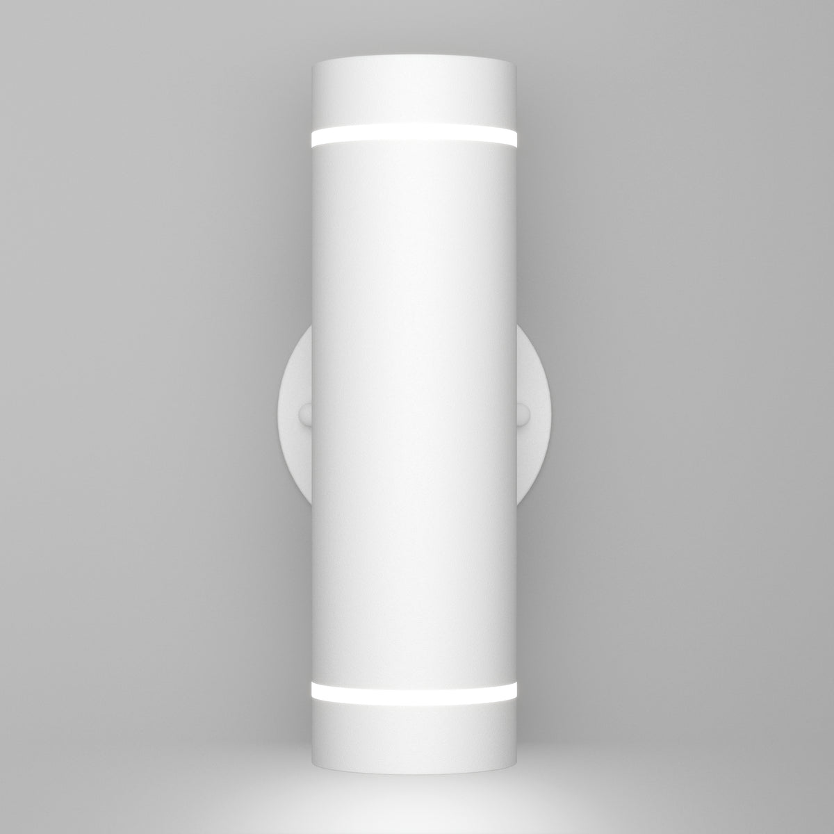 A modern cylindrical wall light fixture with a matte white finish, mounted vertically on a round wall plate, emitting light from narrow openings at the top and bottom. The background is plain and light gray.