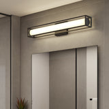 A modern bathroom features a rectangular mirror mounted on a gray wall, with a sleek, horizontal LED vanity light above it. Part of a plant and a towel hanging on the wall are also visible.