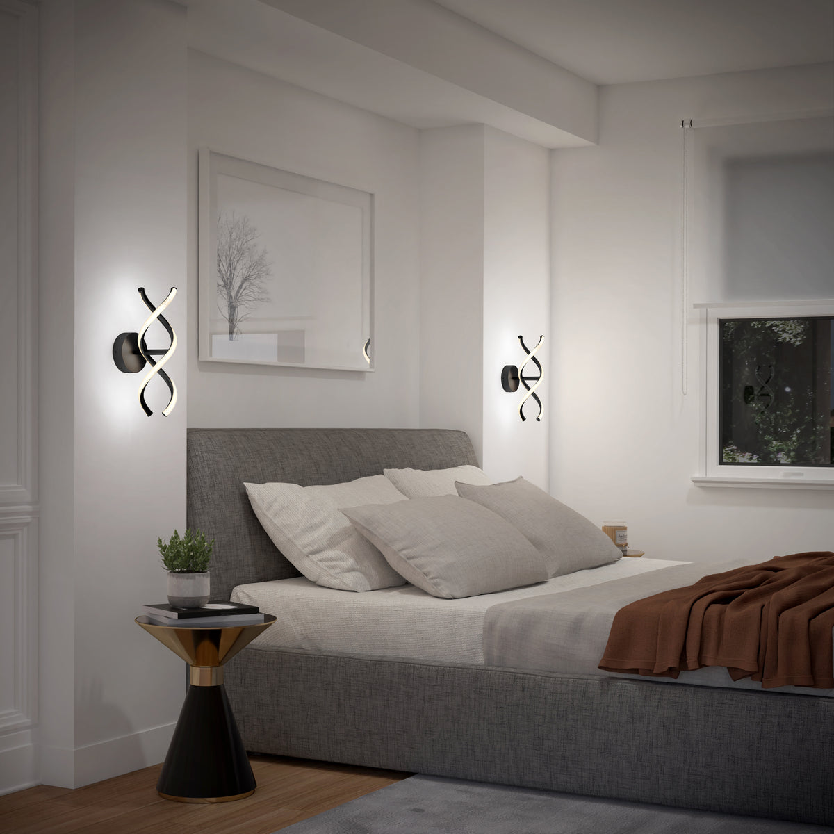 Modern bedroom with a gray upholstered bed, neutral bedding, and a brown throw. Two abstract wall lights flank the bed. A small round side table with a potted plant sits beside the bed. Minimalist decor and a window are visible.