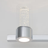 A modern wall-mounted light fixture with a cylindrical glass shade containing bubbles and a metallic silver base, emitting a soft white glow.