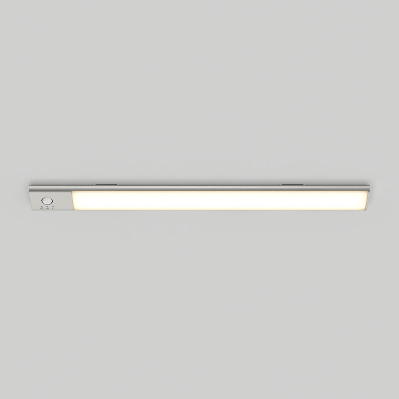 The Artika Outline under cabinet LED light 3CCT, a slim rectangular fixture, is mounted on a plain light gray ceiling. It emits a soft, even glow when turned on and features a small control button at one end.