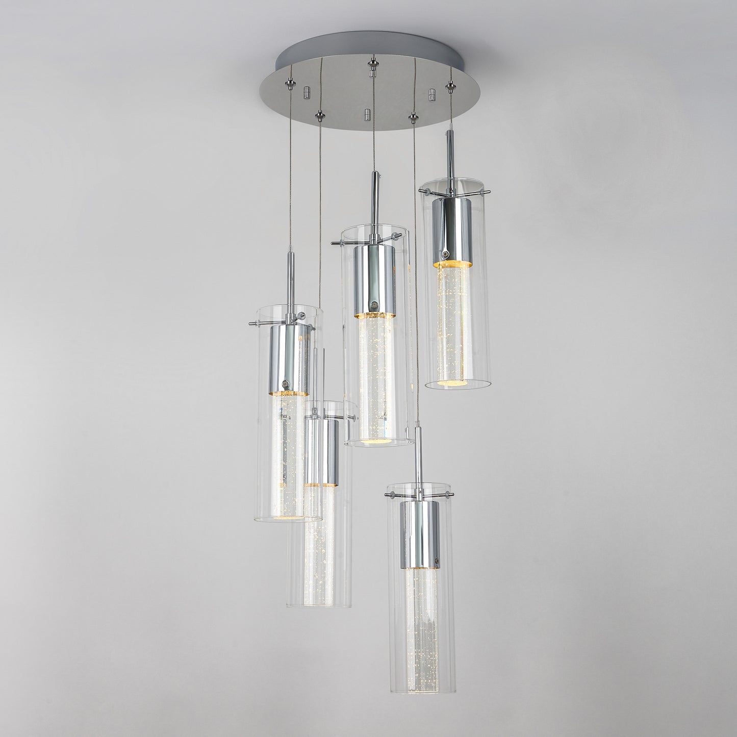 The Artika Essence 5-light LED pendant features five cylindrical glass fixtures at varying heights on a round chrome-accented base, showcasing visible LED filaments for a modern look.