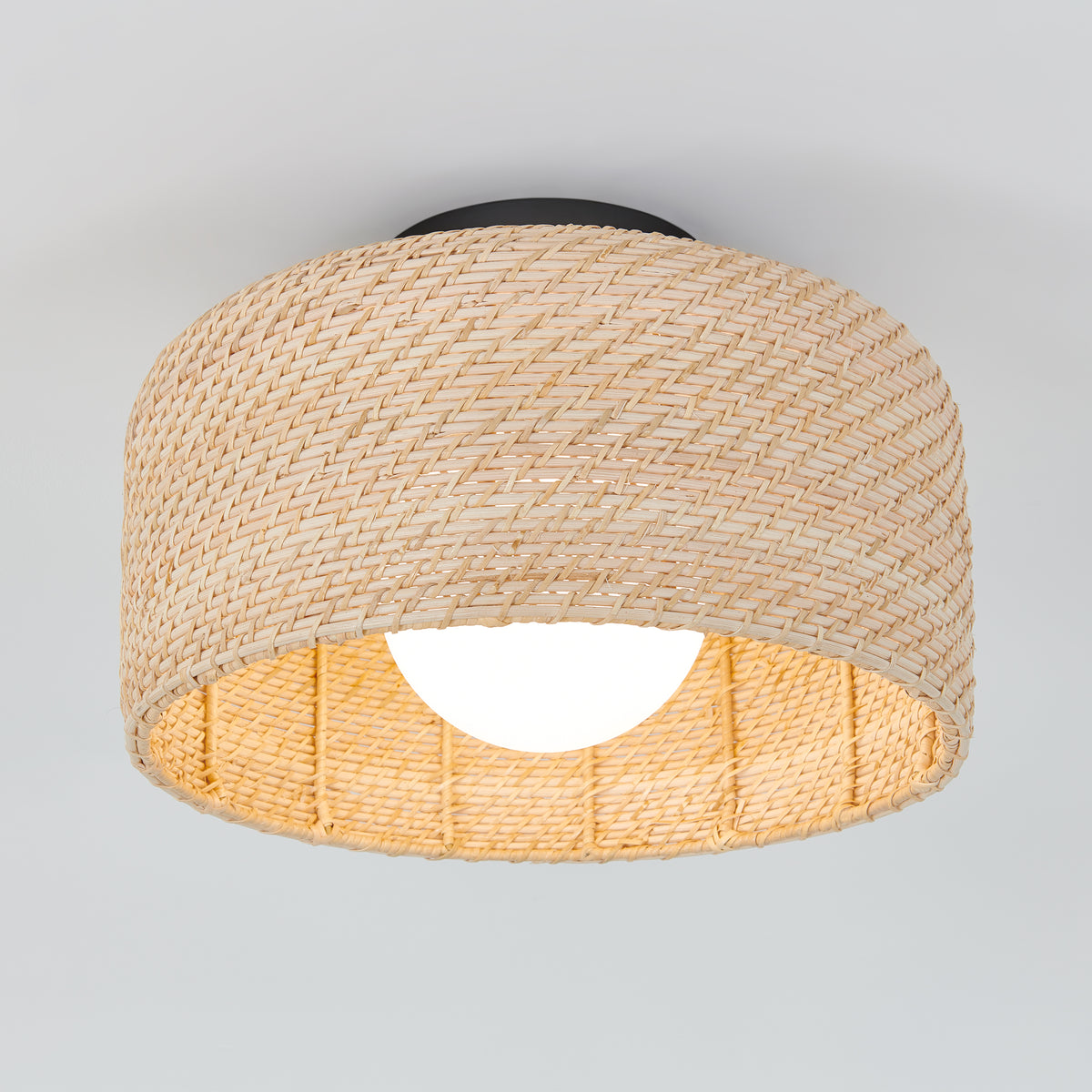 A ceiling light fixture with a woven rattan shade, featuring a round, exposed bulb inside. The natural-colored material creates a warm, textured look against a plain white ceiling.