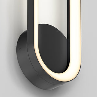 Close-up of the Artika Aiden modern LED indoor-outdoor wall light 5 CCT, featuring a black circular base and a smooth curved illuminated strip in a partial oval shape, mounted on a light-colored wall.