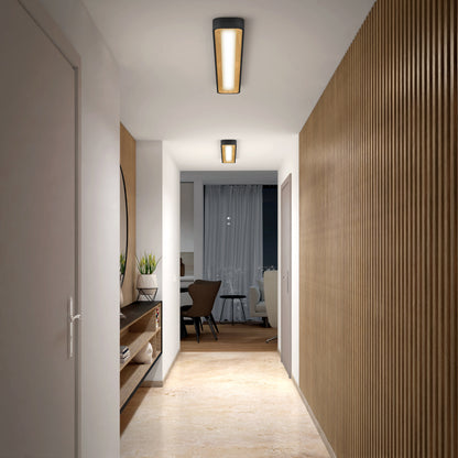 A modern hallway with wooden floors and slatted wood panels is lit by the Artika Alton 48 in. LED flush mount light. A side shelf holds plants and decor, leading to a dining area with dark chairs and a round mirror.