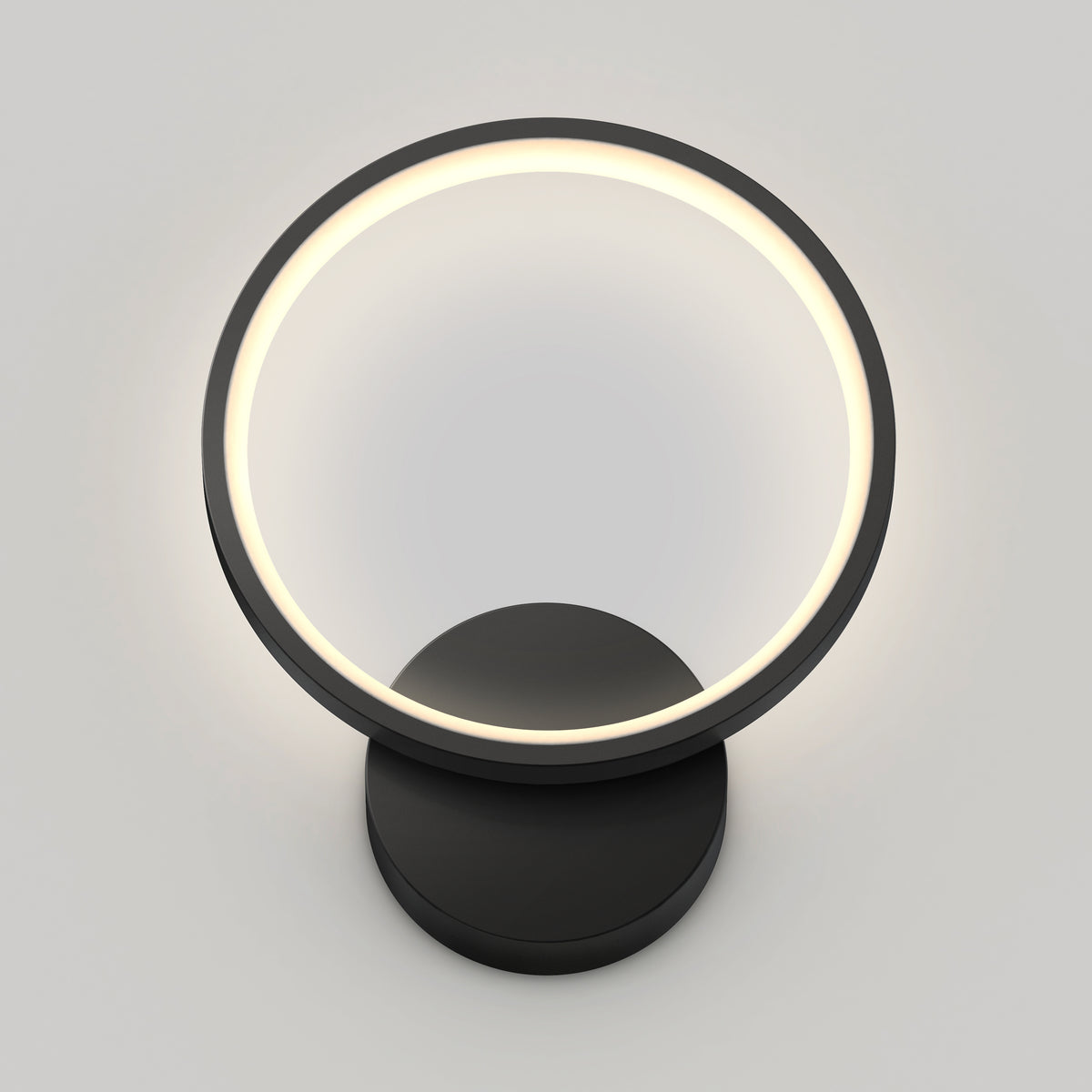 A modern circular wall lamp with a black base and a glowing white ring, mounted on a plain light gray wall.