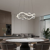 A modern dining room with a round marble table, brown chairs, a gray sofa, and a sculptural LED chandelier hanging from the ceiling. Large windows provide natural light, and the kitchen area is visible in the background.