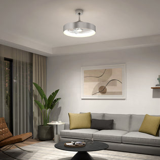 A modern living room with a gray sofa, green and beige pillows, a round black coffee table, potted plant, abstract wall art, and the Artika Austin 23 in. LED modern ceiling fan with remote overhead. Sunlight streams through large windows.