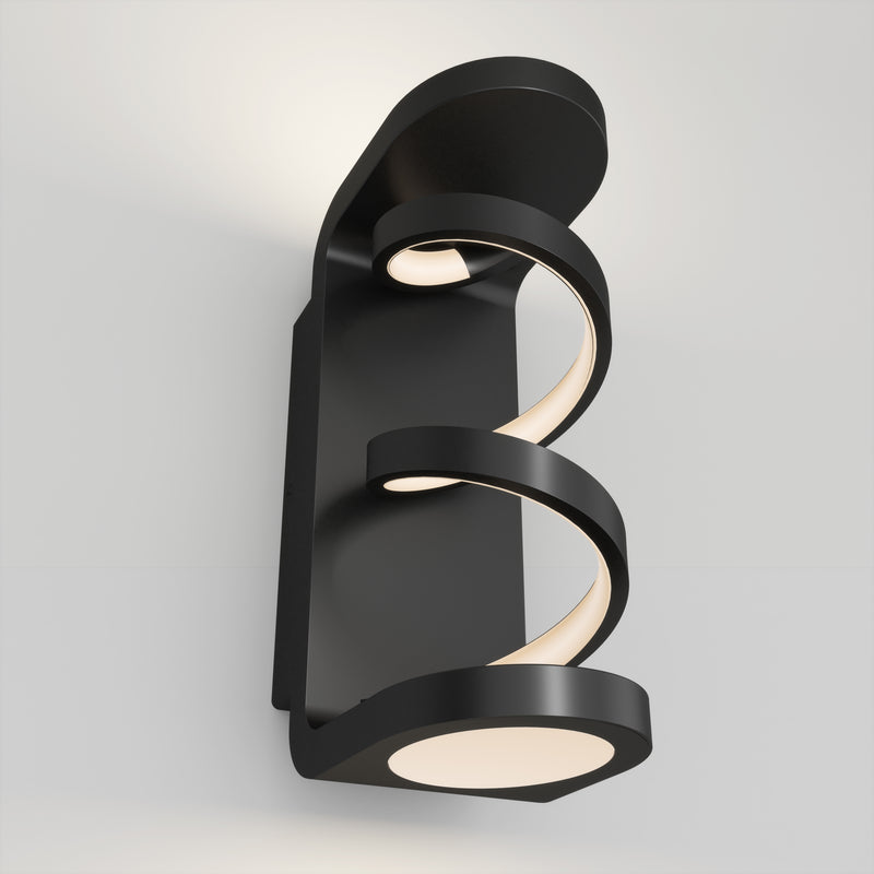 The Artika Swirl indoor-outdoor LED wall light features two spiral, glowing strips on a modern black rectangular base, casting a soft white glow on your wall.