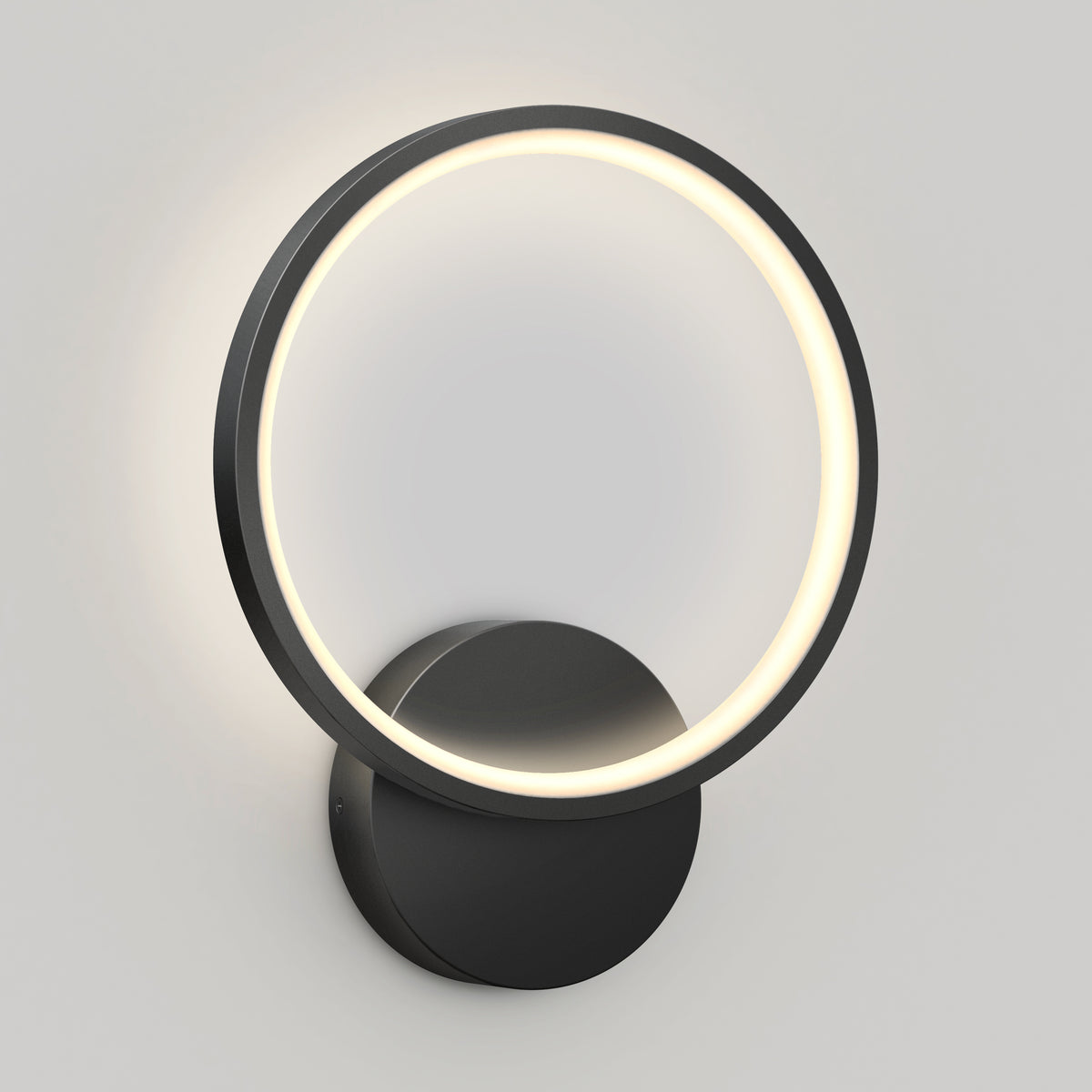 The Artika Solis modern LED indoor-outdoor wall light 5 CCT features a circular LED ring with a black frame on a round base, casting a soft glow against a light gray wall.