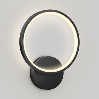 The Artika Solis modern LED indoor-outdoor wall light 5 CCT features a circular LED ring with a black frame on a round base, casting a soft glow against a light gray wall.