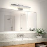 Modern bathroom with a large mirror above a speckled countertop, a rectangular sink, a potted plant, folded towels, and a sleek wall-mounted light fixture. A shower with a glass door is visible in the reflection.