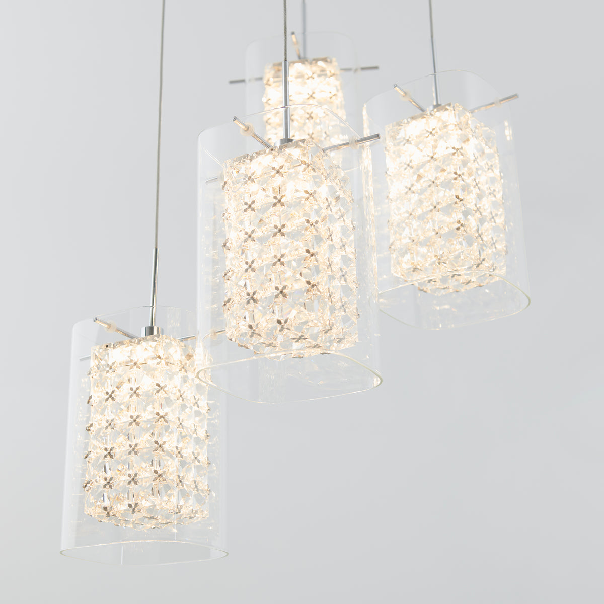 Four modern pendant lights with cylindrical glass shades and intricate, crystal-like inner patterns hang from the ceiling against a light gray background.