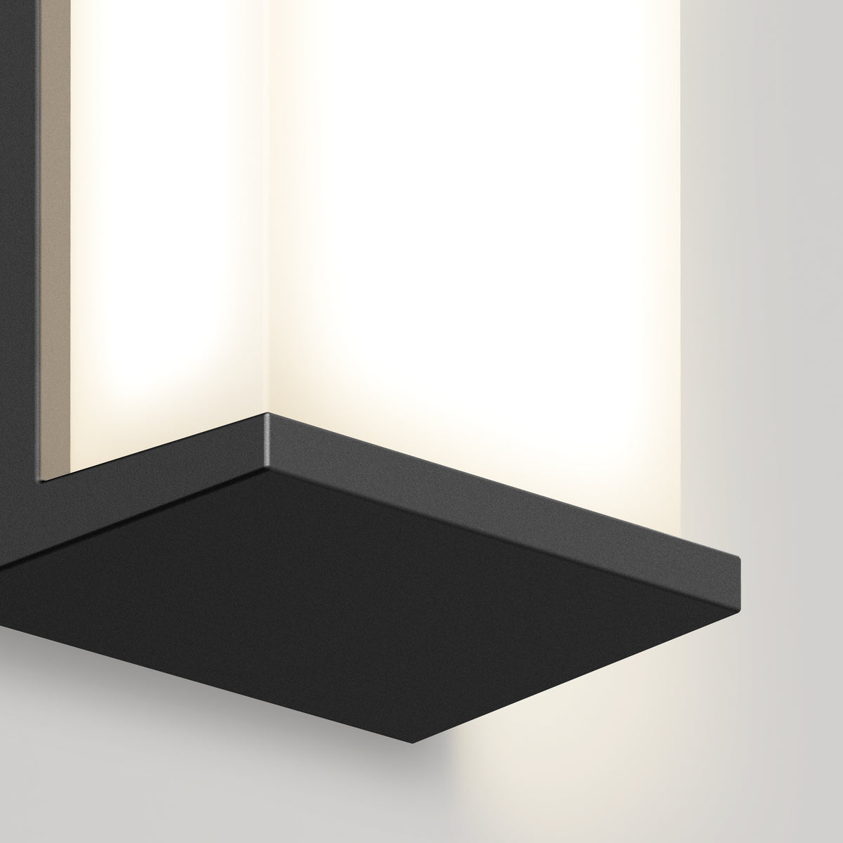 Close-up of a modern wall-mounted light fixture with a rectangular black metal base and a frosted glass shade, glowing softly against a light-colored wall.