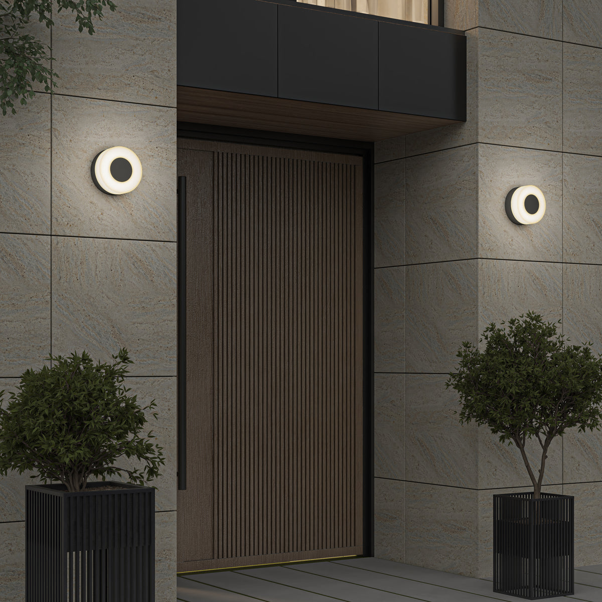 A modern entrance with a wooden door, light stone tile walls, two circular wall lights on either side, and two potted plants in black containers flanking the doorway.